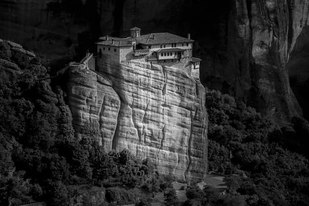 A Byzantine monastery perched on top of a tall sandstone rock pillar at Meteora in central Greece, with forested hills behind it in late afternoon light